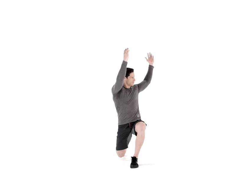 A close-up photo of a person performing a reverse lunge with both arms reaching overhead in a home workout space, showing hip alignment and a stable front knee tracking over the midfoot