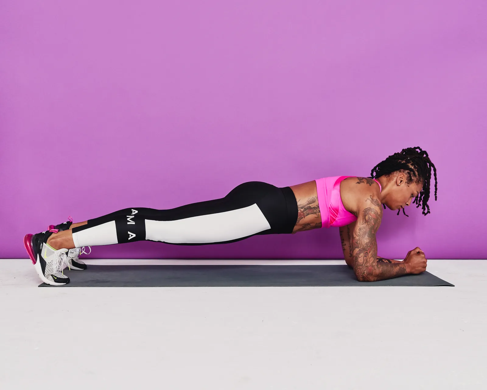 A close-up view of a person holding a forearm plank with elbows stacked under shoulders, forearms parallel, ribs stacked over the pelvis, and body in a straight line