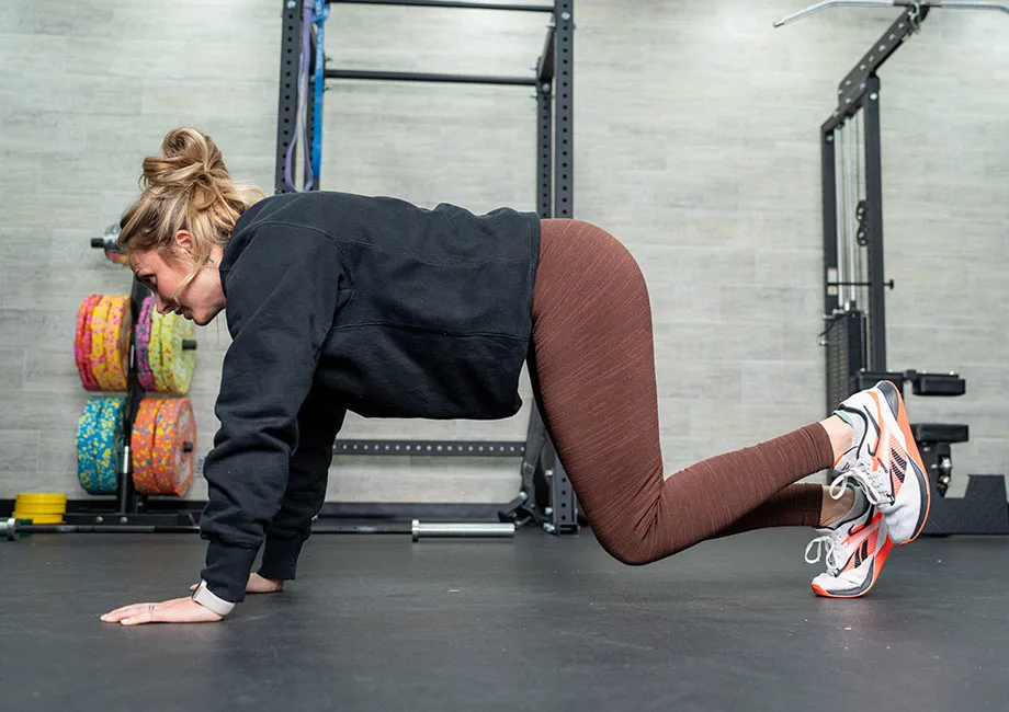 A close-up view of a person on hands and knees hovering both knees a few inches off the floor, back flat, ribs stacked, and shoulders stable