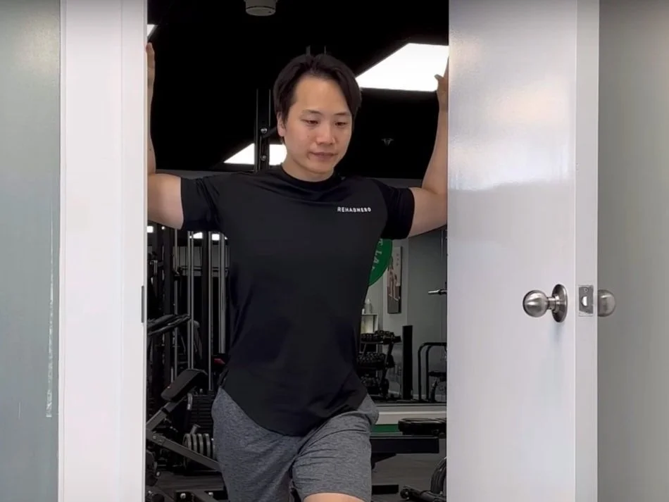 A person doing a chest stretch with one forearm against a doorway, gently turning away to open the chest