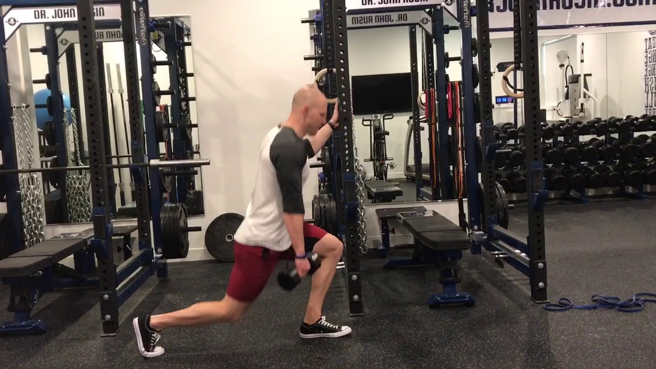 A person doing an assisted reverse lunge while holding the back of a chair for balance in a home setting