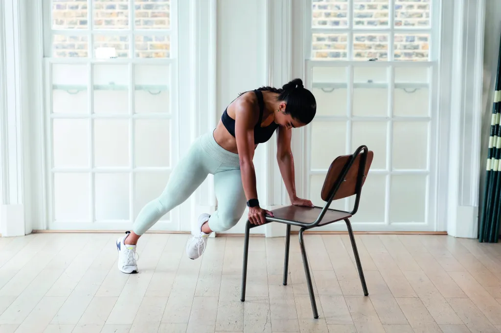 A person doing slow mountain climbers with hands on a sturdy chair seat, feet stepping back on the floor