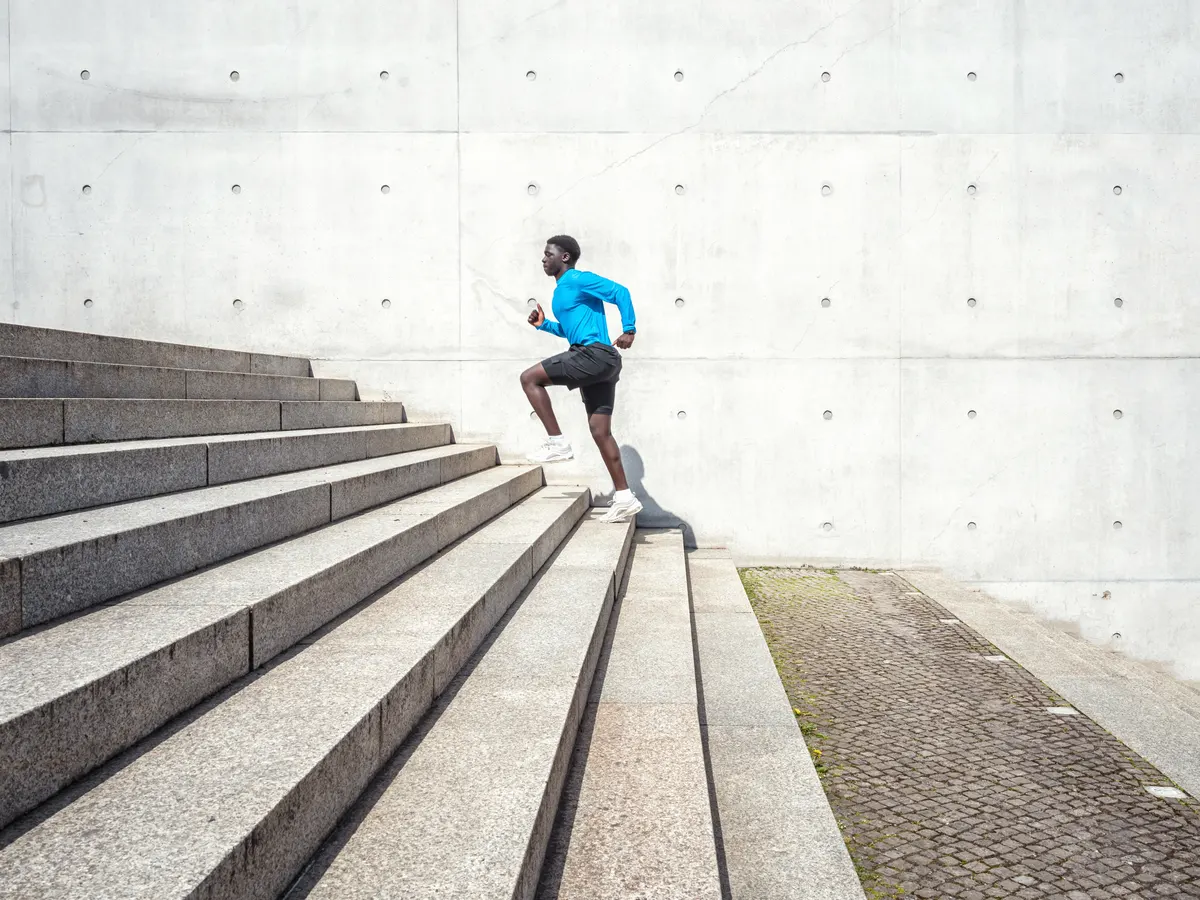 A person doing step-ups on a single stair at home, one foot planted on the step and torso upright