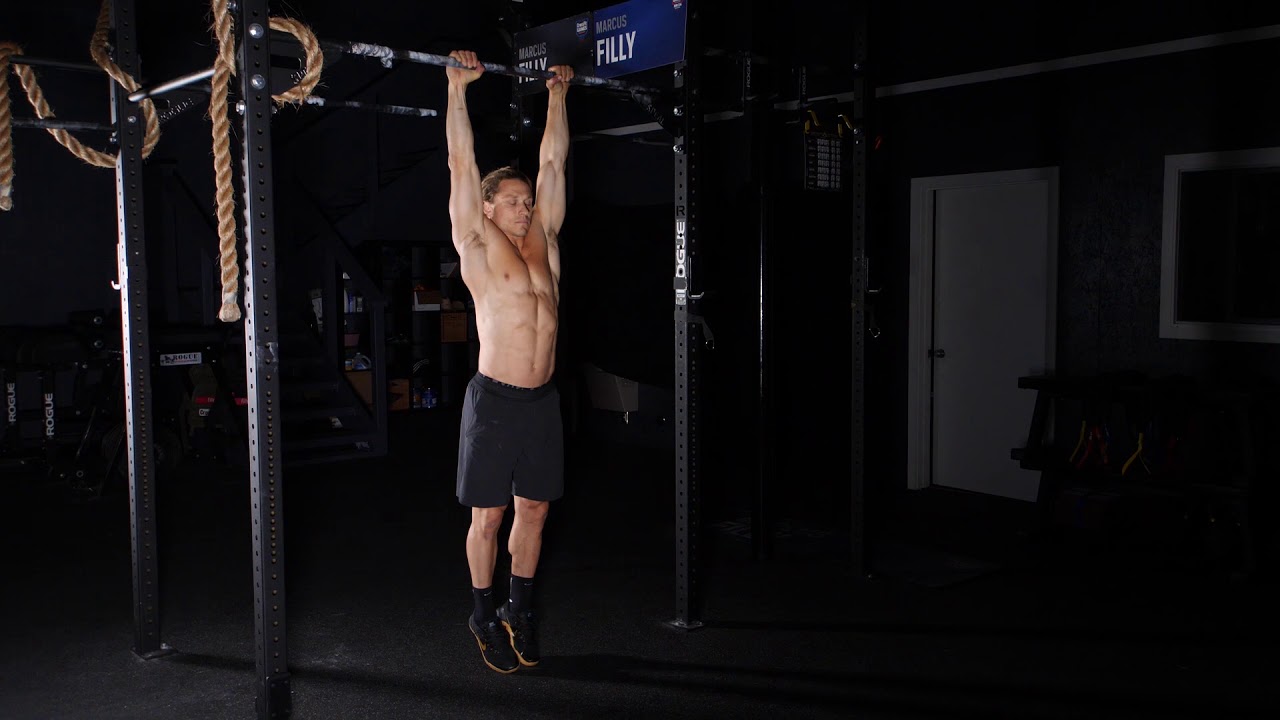 A person hanging from a doorway pull-up bar performing a scapular pull, shoulders depressed and body lifted slightly without bending the elbows