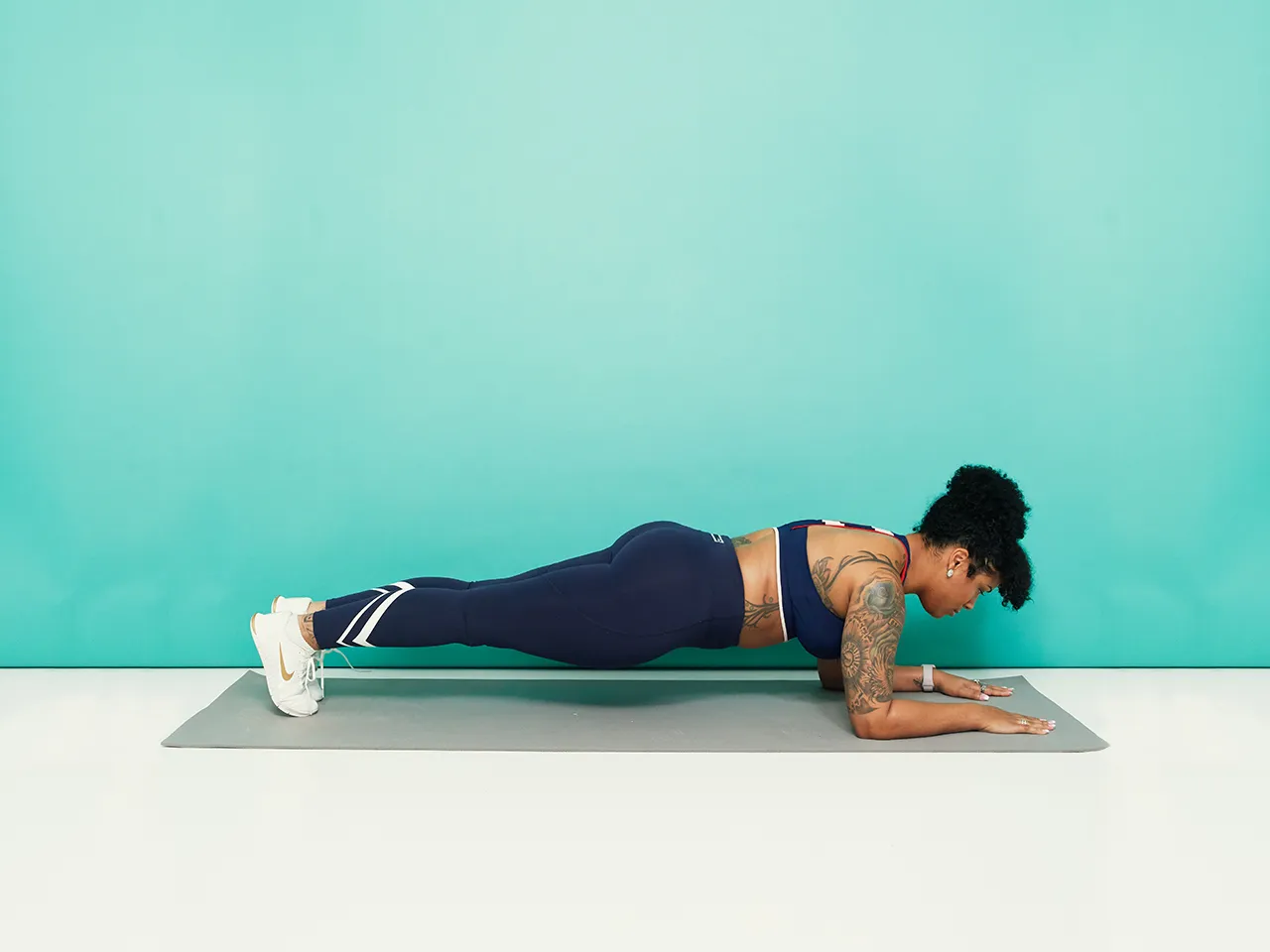 A person holding a forearm plank on a yoga mat with relaxed shoulders and a neutral spine in a small apartment living room