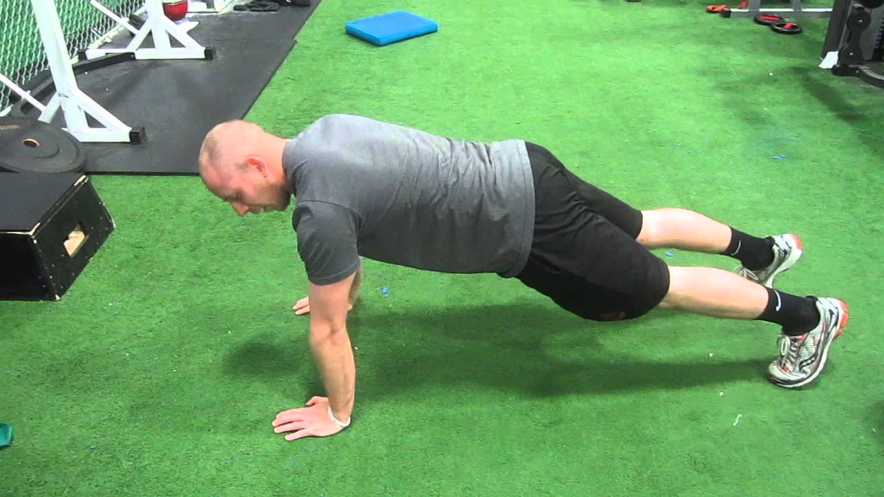 A person holding a high plank position on a yoga mat, arms straight while pushing the upper back slightly upward for a scapular push-up