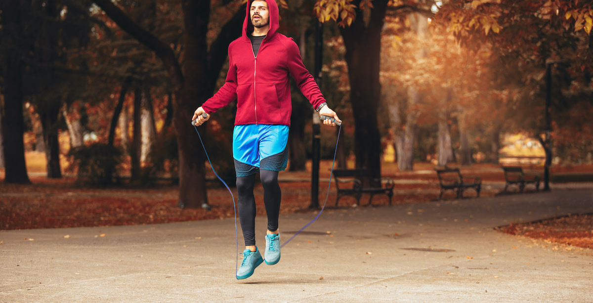 A person holding a jump rope in a small apartment living room, with sneakers and a cleared workout space