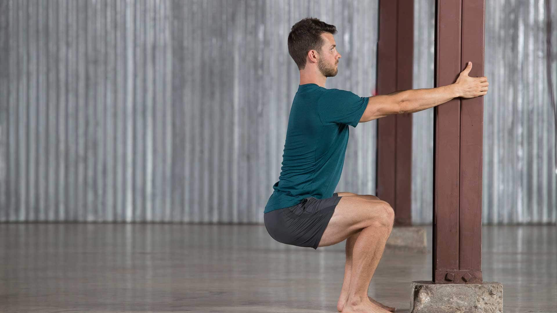 A person holding the back of a sturdy chair while sitting into a deep squat, heels supported and chest lifted