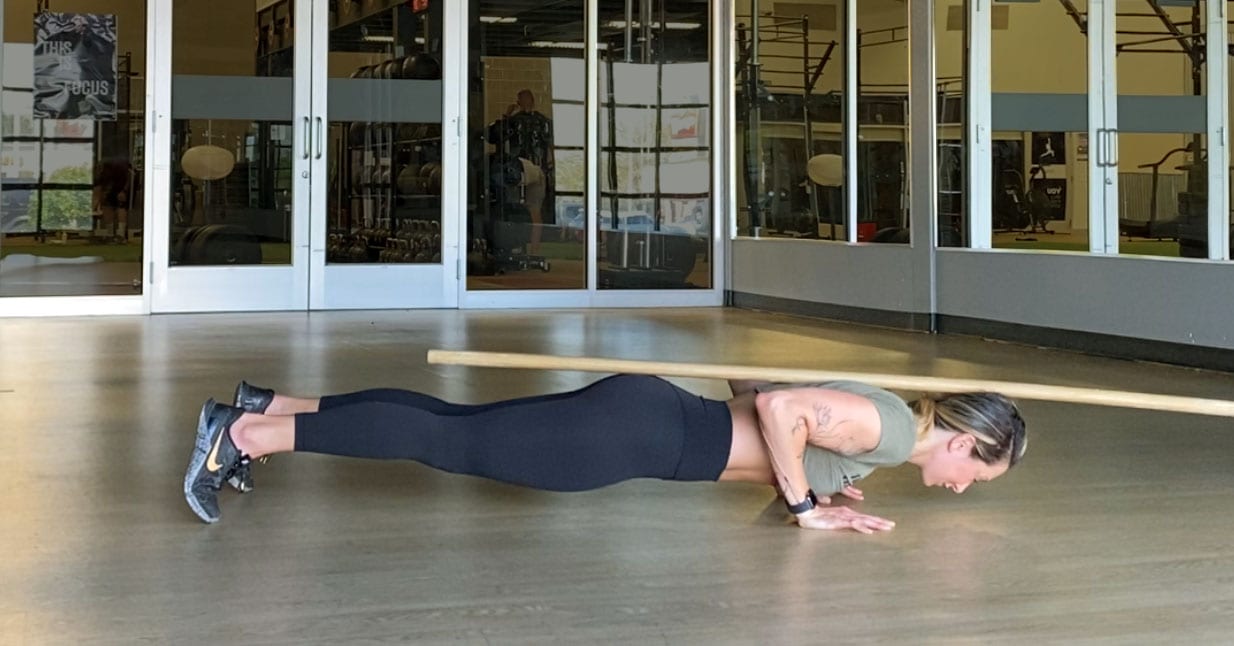 A person holding the bottom position of a push-up a few inches above the floor with a straight body line