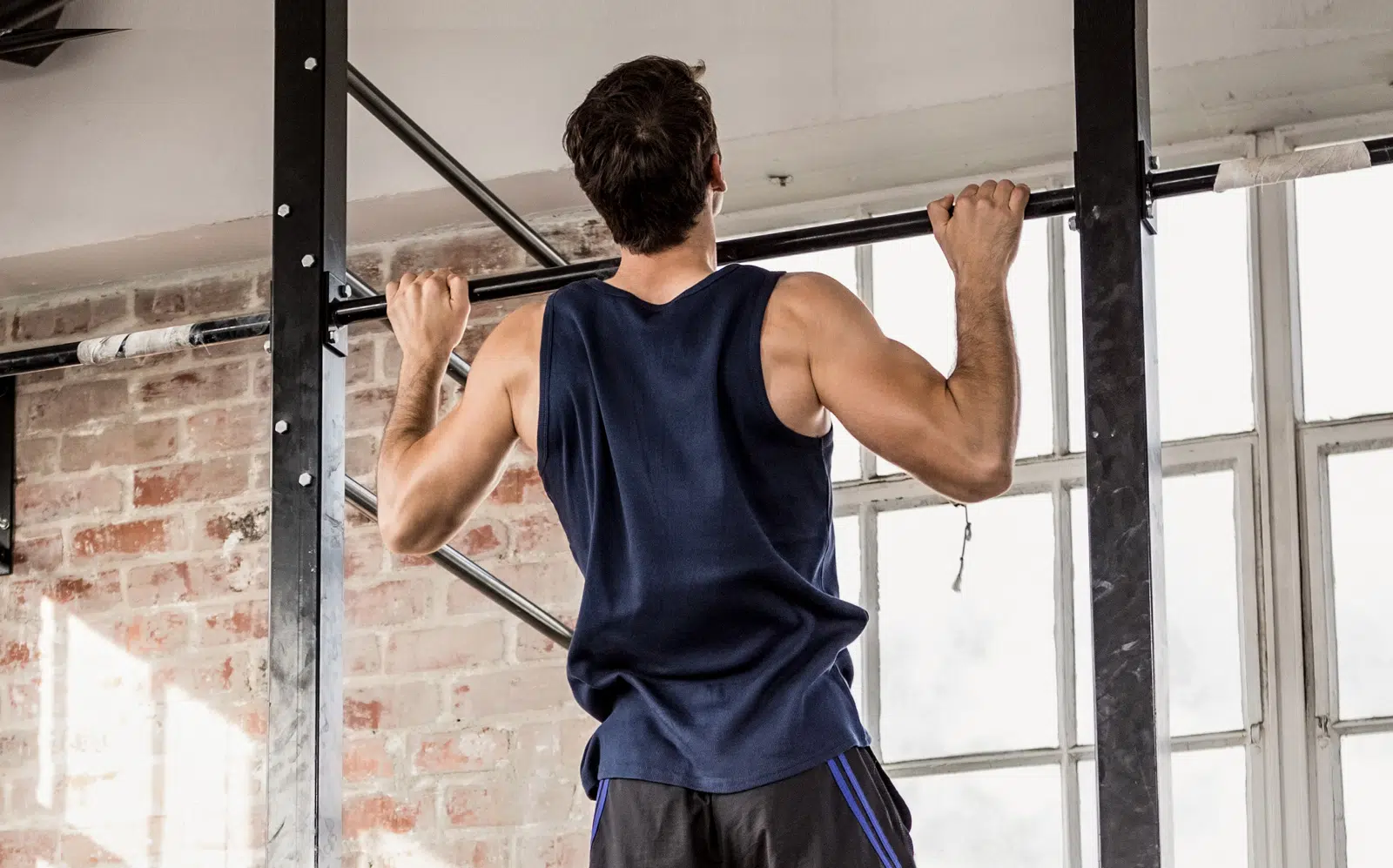 A person holding the top of a pull-up on a doorway bar with chin above the bar and elbows bent, body steady and controlled