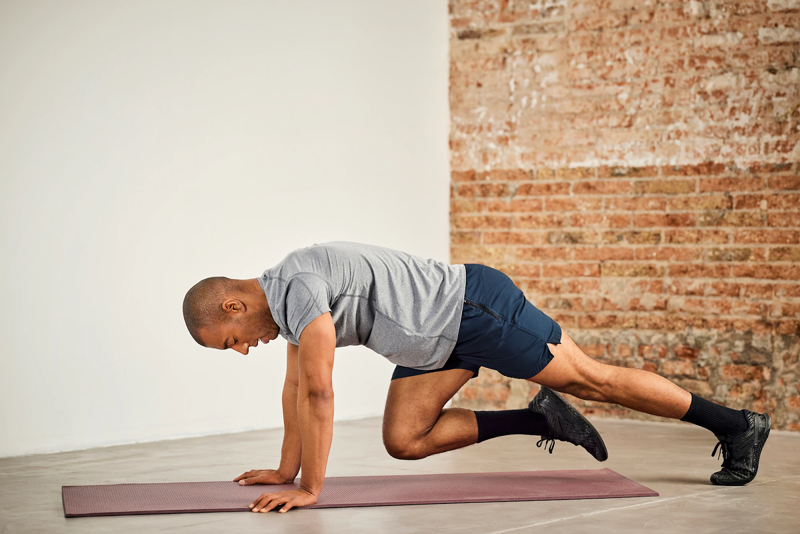 A person in a high plank bringing one knee toward the chest slowly with control, shoulders stacked over wrists and torso steady