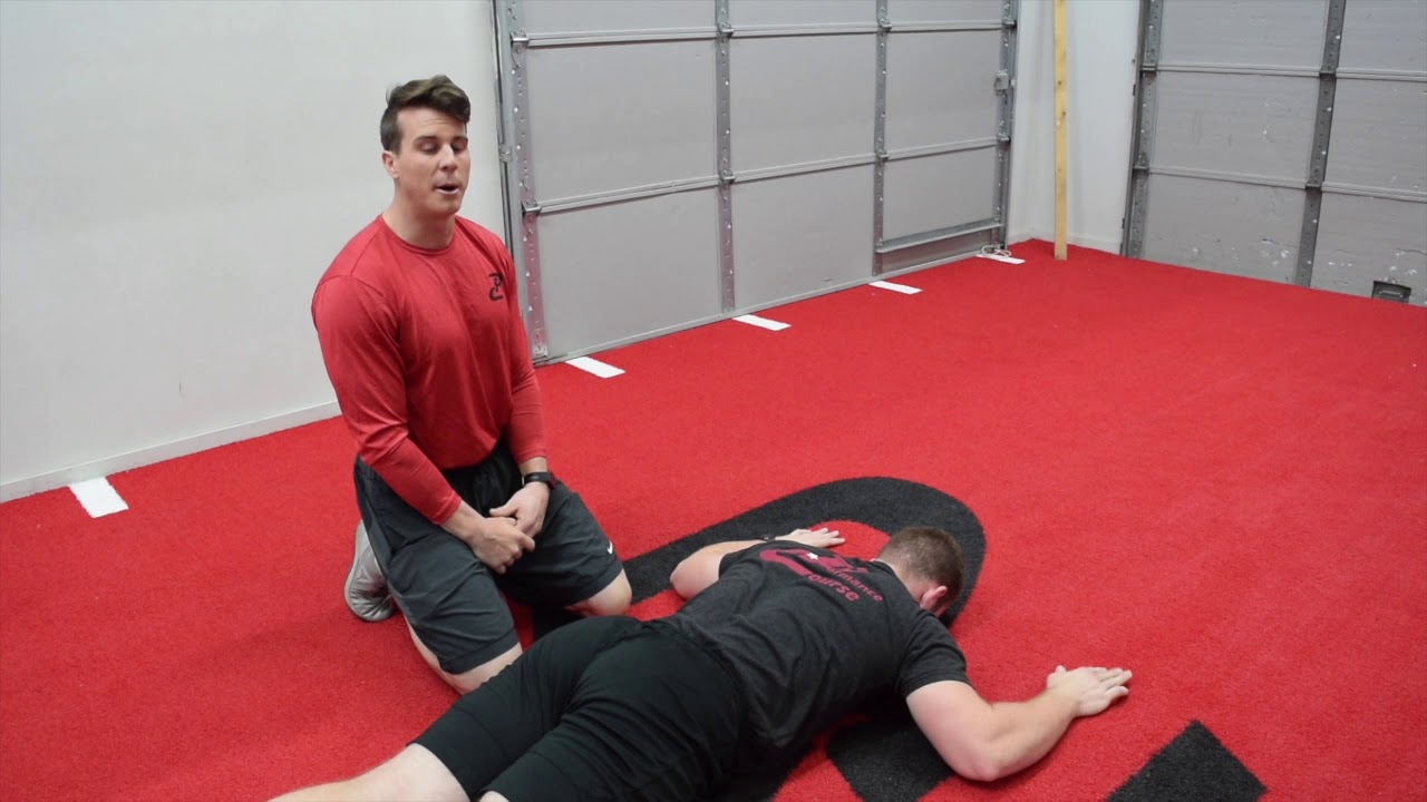 A person lying face down on a mat performing a prone Y raise with straight arms overhead, lifting slowly and keeping the neck neutral