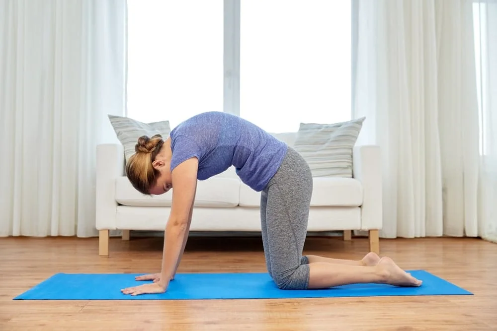A person on hands and knees on a mat moving through a gentle cat-cow stretch, warming up the spine before core training