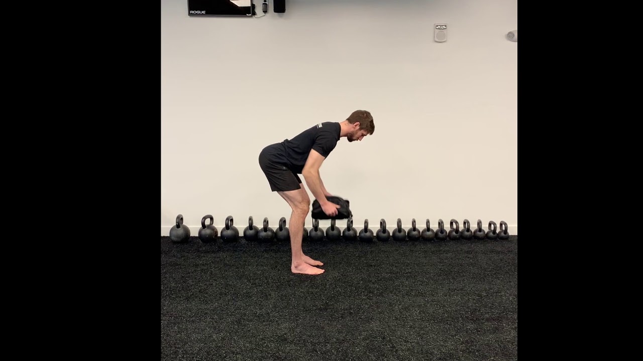 A person performing a bent-over row in a living room using a loaded backpack as a weight, with a neutral spine and hips hinged back