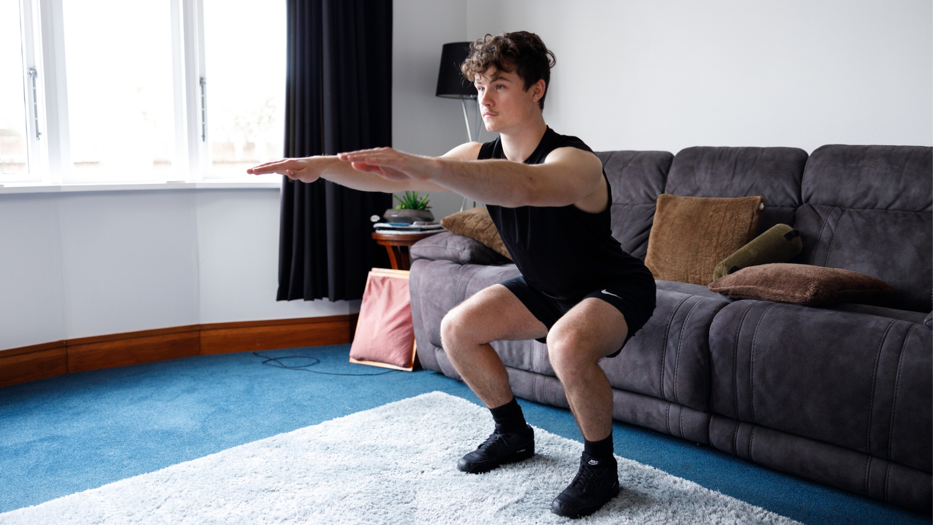 A person performing a box squat by lightly touching the edge of a couch with their hips before standing back up