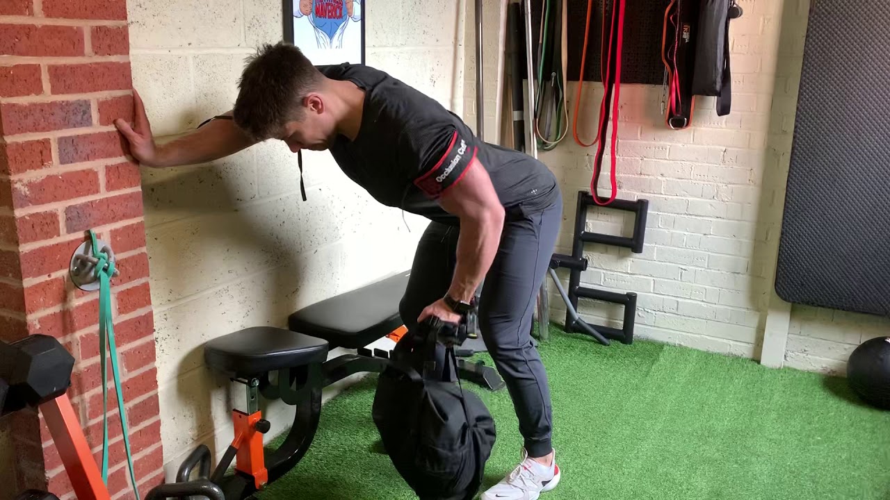 A person performing a controlled bent-over row at home using a backpack as weight, keeping a flat back and pulling toward the ribs