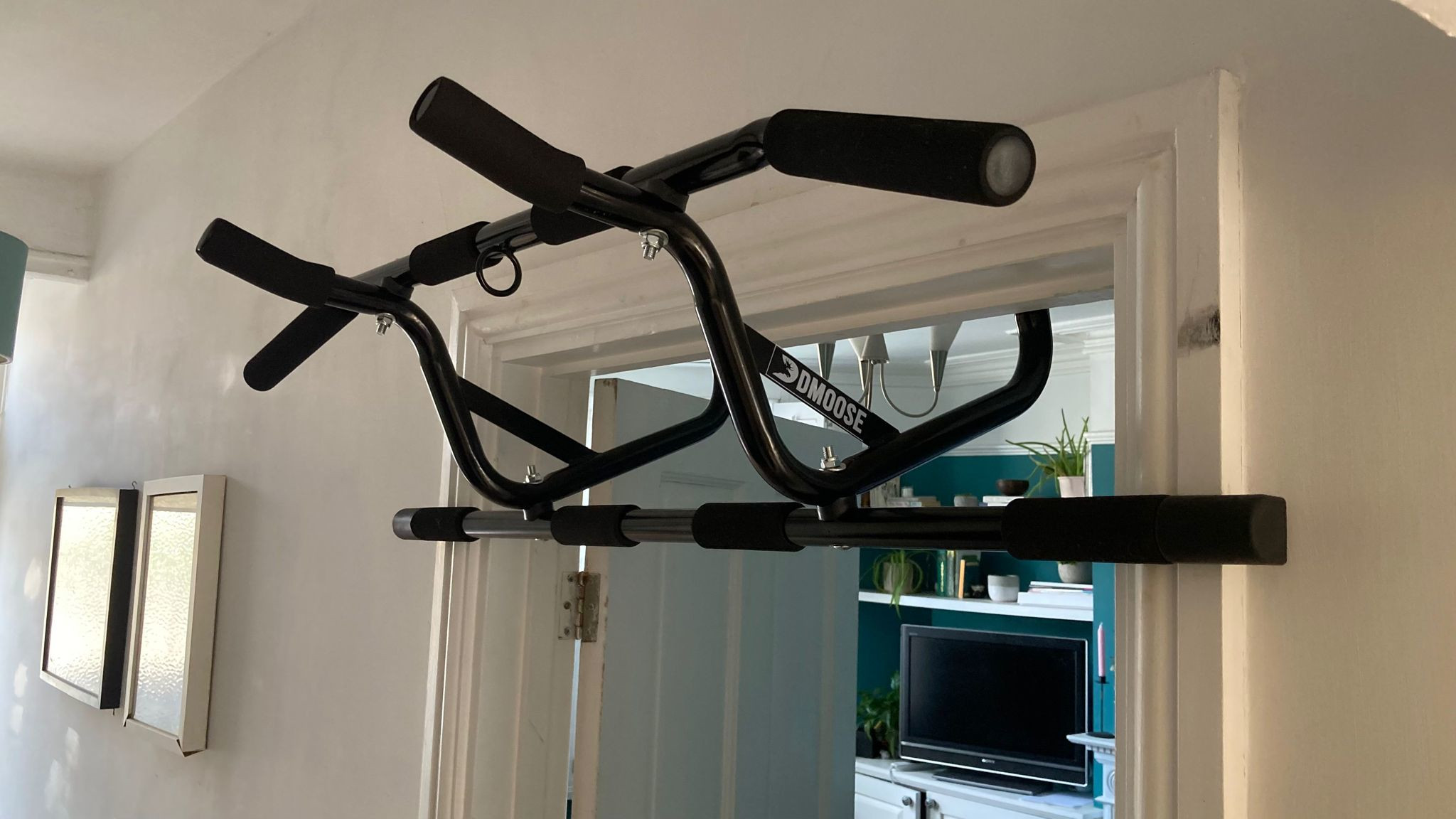 A person performing a dead hang from a doorway pull-up bar, arms fully straight, legs slightly bent, with a controlled body position