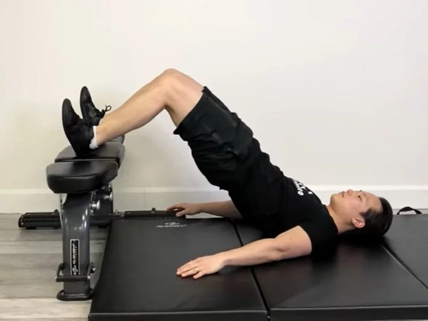 A person performing a feet-elevated glute bridge with heels resting on a couch, shoulders on the floor and hips lifted