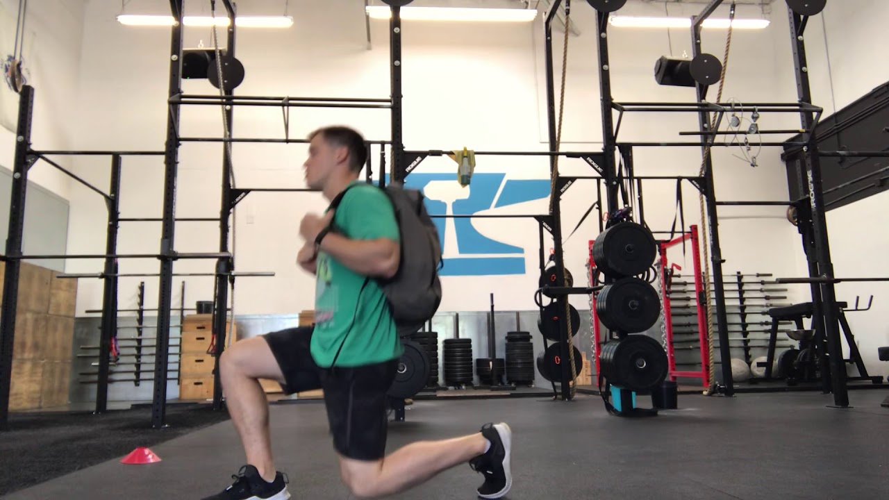 A person performing a reverse lunge in a small apartment while wearing a backpack for added resistance