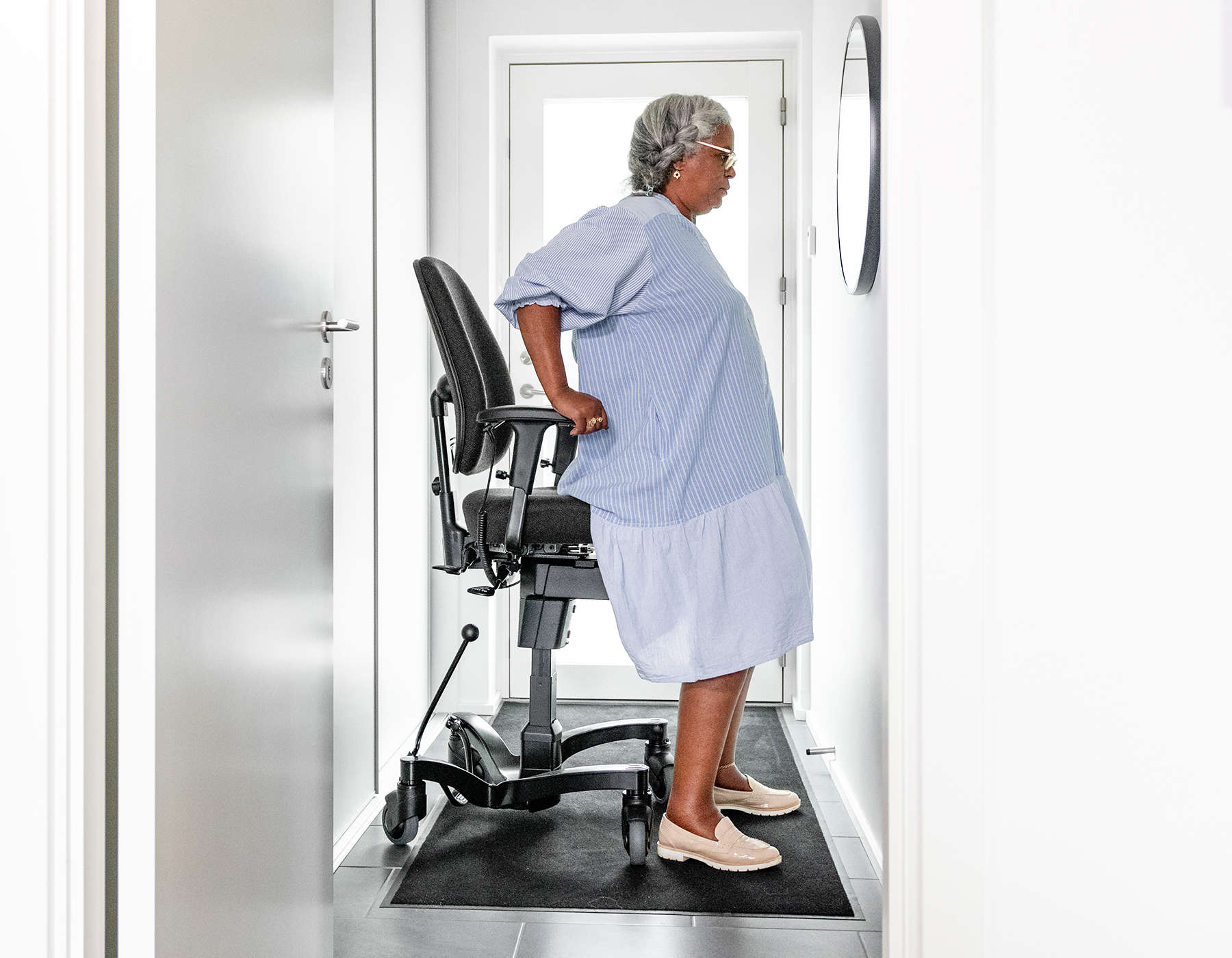 A person rising from a chair using a controlled sit-to-stand movement, feet hip-width apart on a living room floor