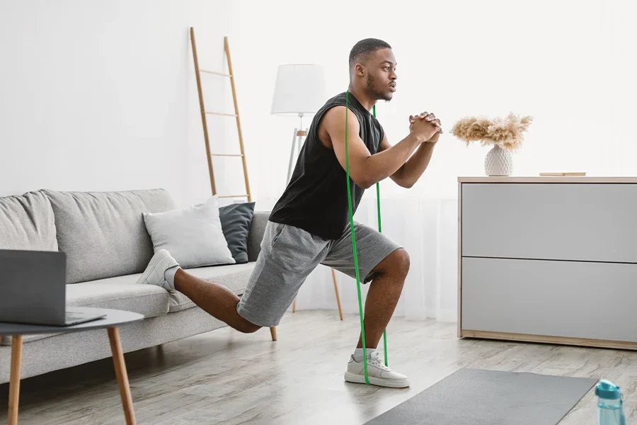 A person setting up a Bulgarian split squat at home with the back foot supported on a couch, using a hand on the wall for balance