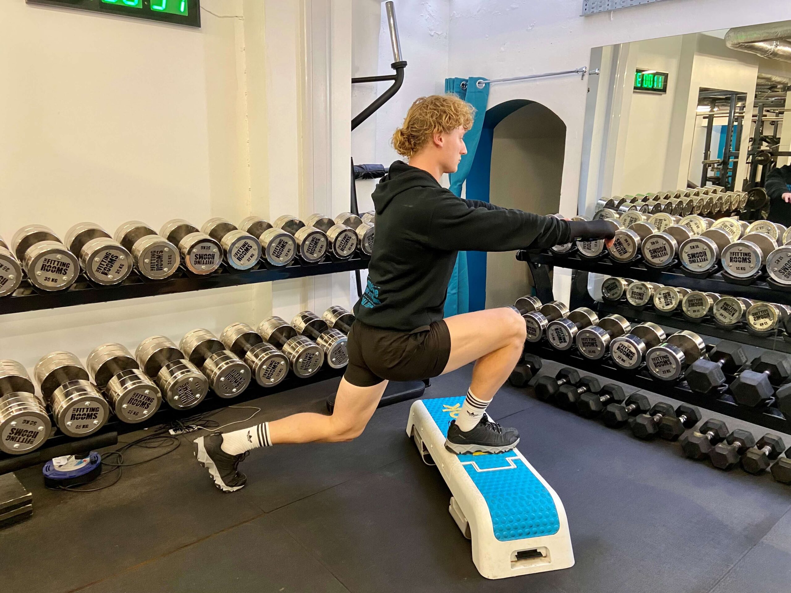 A person standing on a low step platform at home performing a deficit reverse lunge, with the back knee lowering below the level of the front foot