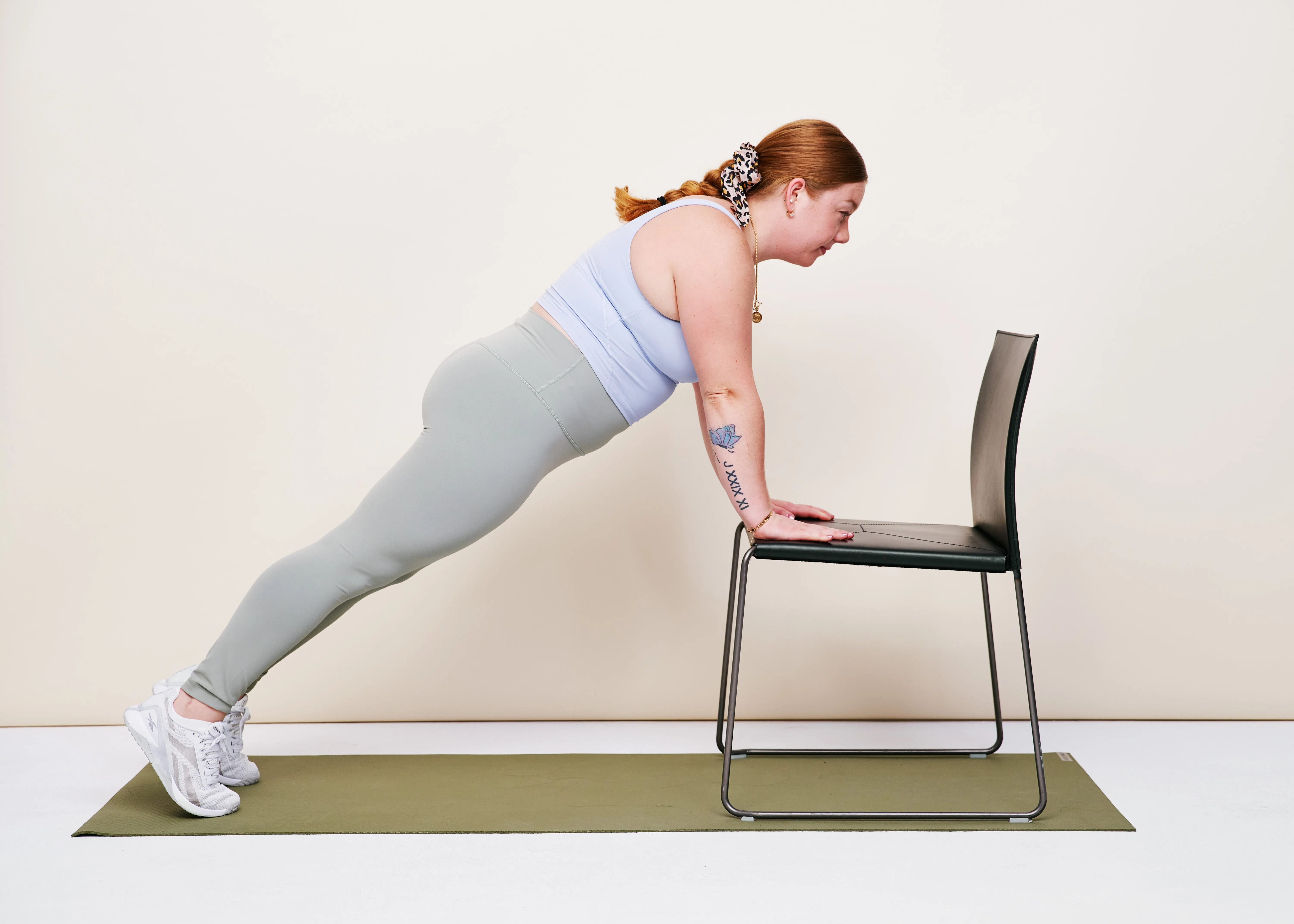 A person using a sturdy dining chair for an incline plank, feet on the floor and hands on the chair seat, body in a straight line