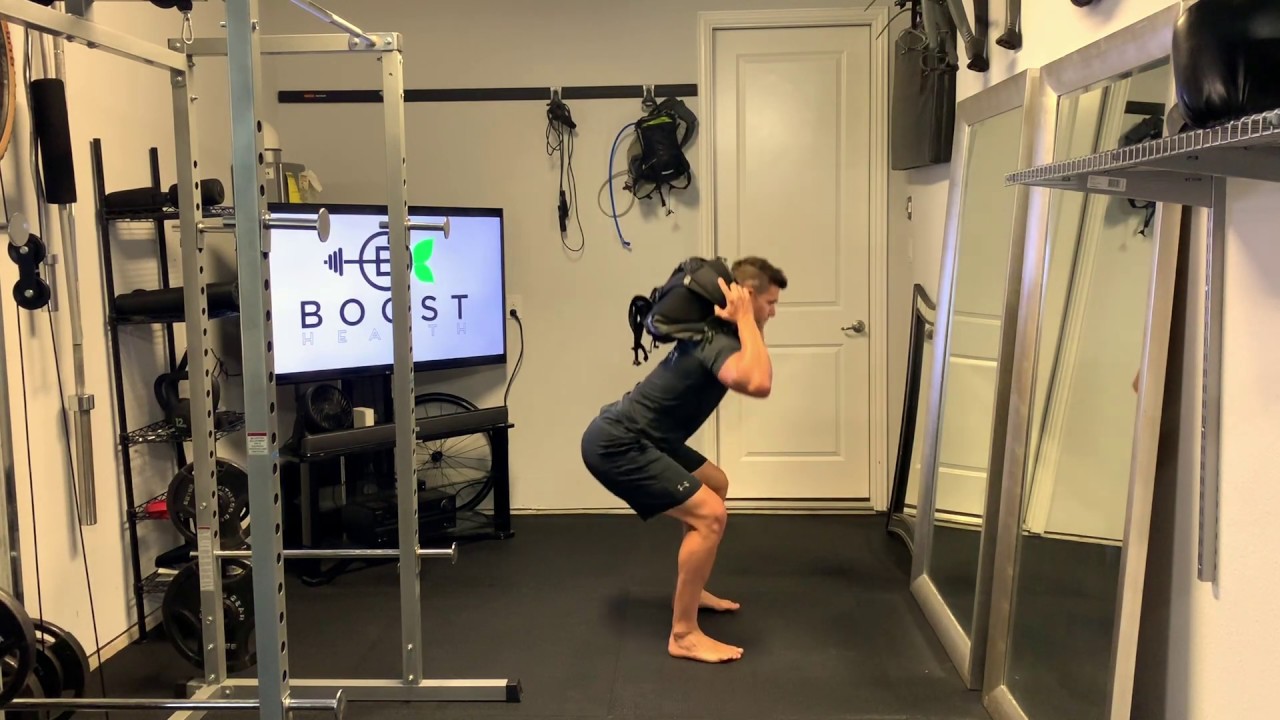 A person wearing a snug backpack while performing a controlled squat in a tidy living room