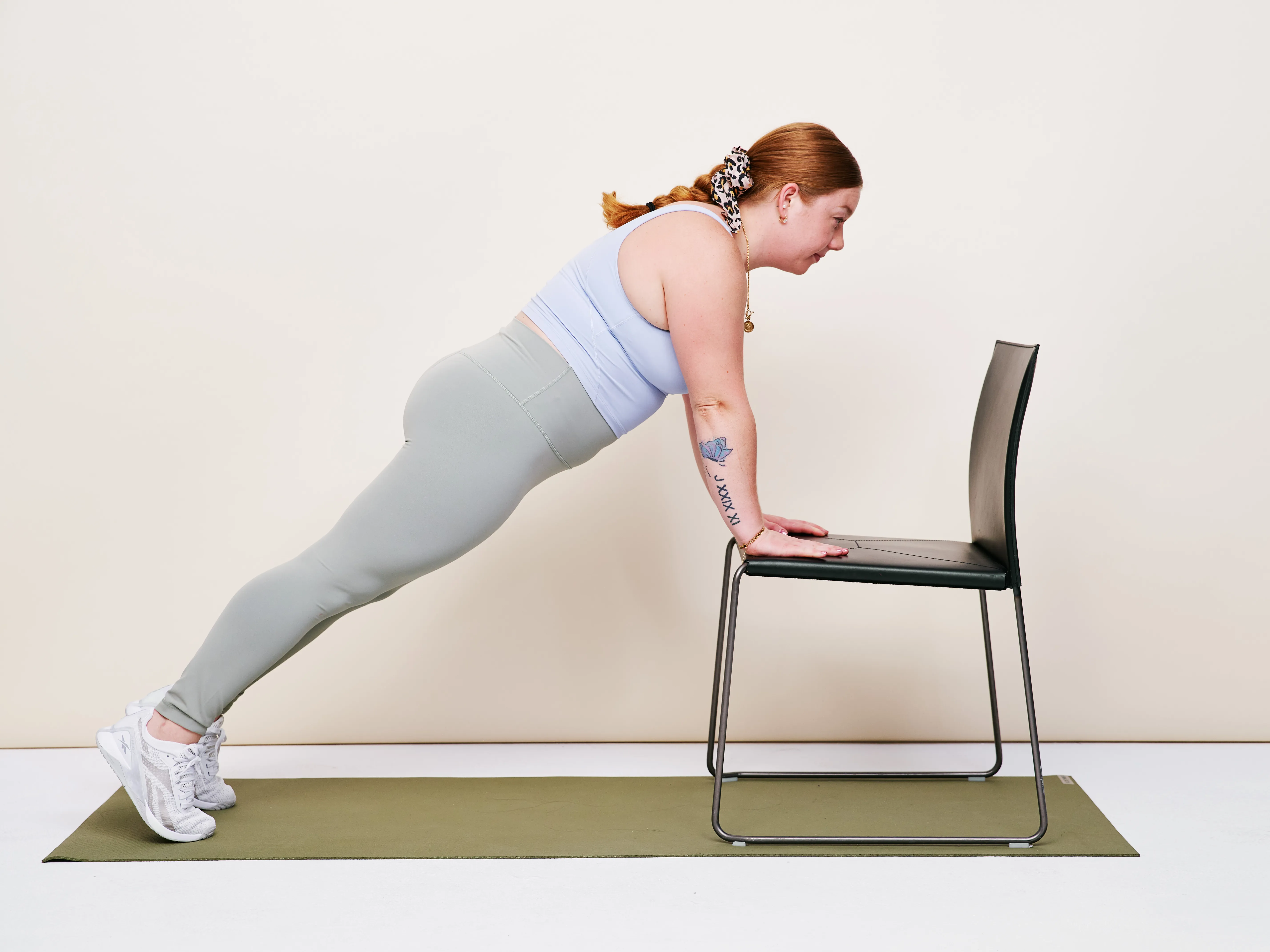 A sturdy dining chair on a hardwood floor beside a yoga mat and a water bottle, set up for a home workout