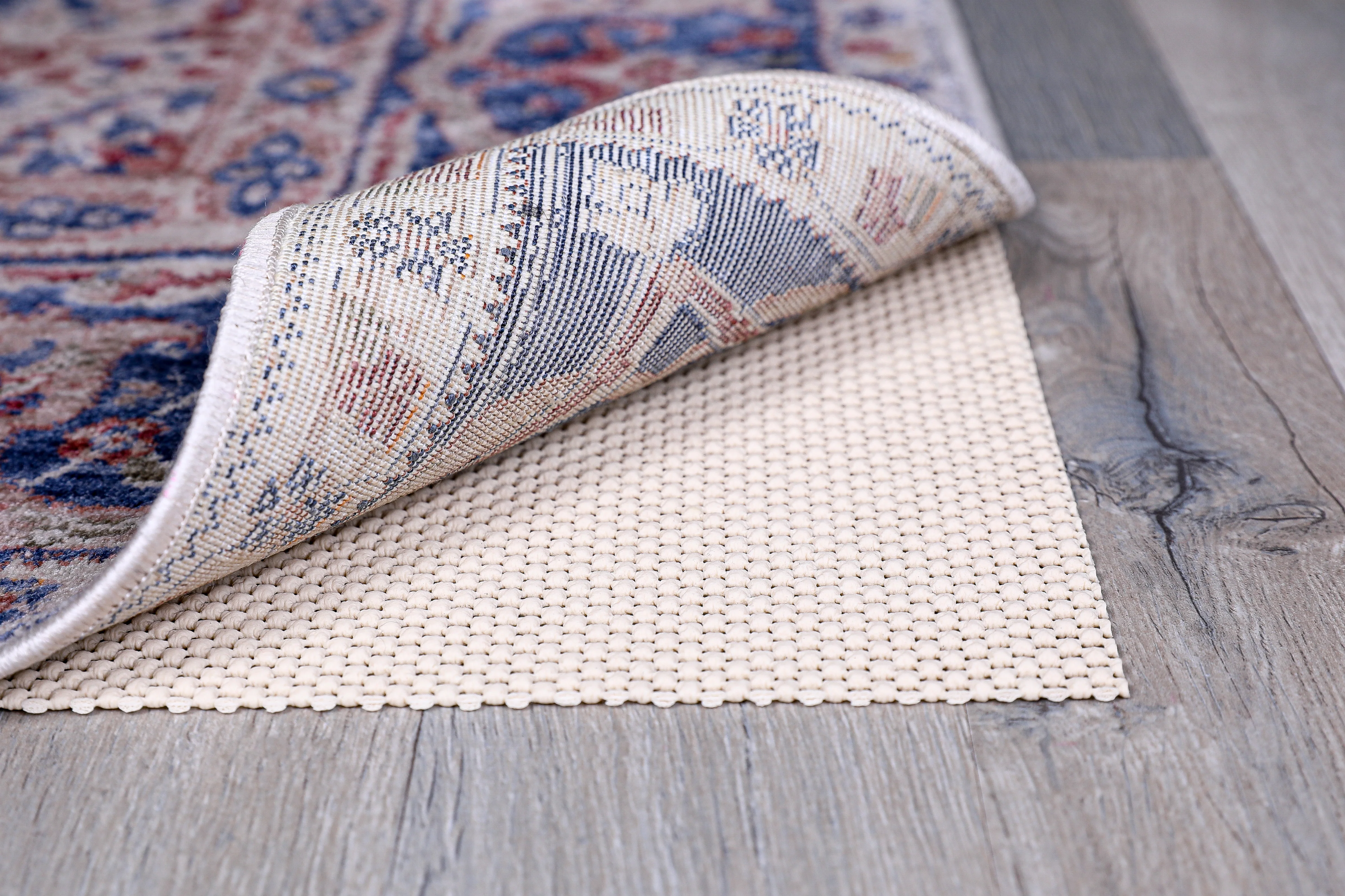 A yoga mat corner lifted to show a non-slip rug pad underneath on a hardwood floor