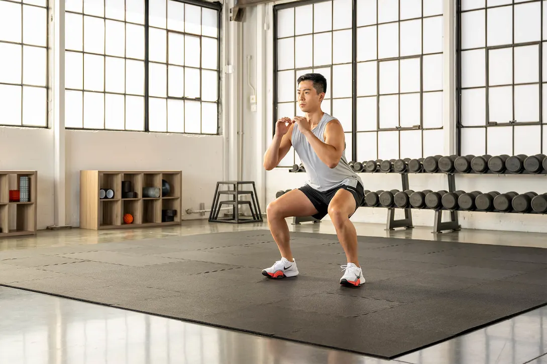 Person landing a squat jump with knees and hips bent and arms forward for balance